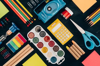 Flat lay composition of colorful school supplies isolated on dark board background clipart