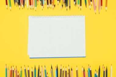Top view of frame of colorful pencils isolated on yellow background with notebook clipart