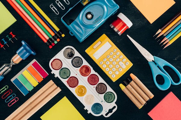 Плоская композиция красочных школьных принадлежностей, изолированных на фоне темной доски
