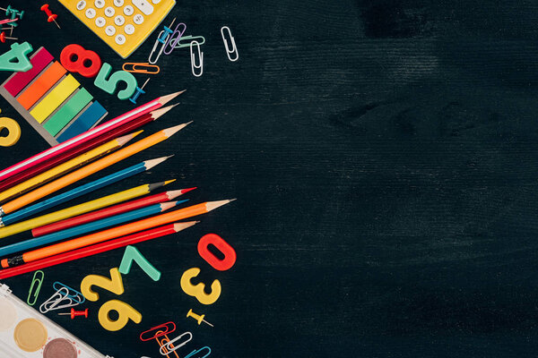 Top view of composition of colorful school supplies isolated on dark board background