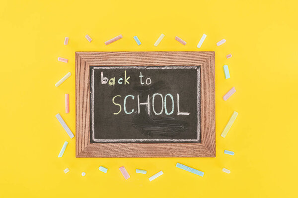 Top view of Back to school inscription on chalk board with chalks isolated on yellow