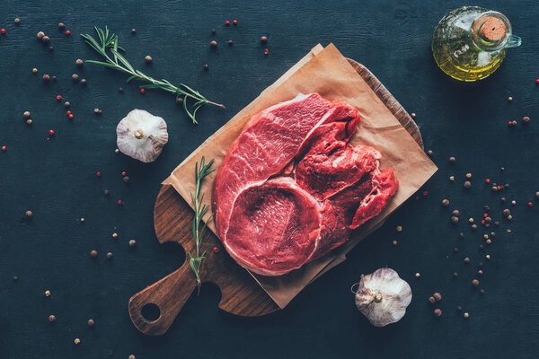 top view of raw steak on parchment paper and cutting board with spices around