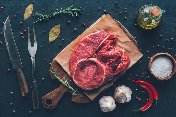 top view of raw steak on parchment paper and cutting board with spices and cutlery around