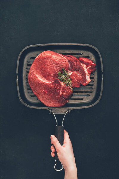cropped shot of woman holding grill pan with raw steak