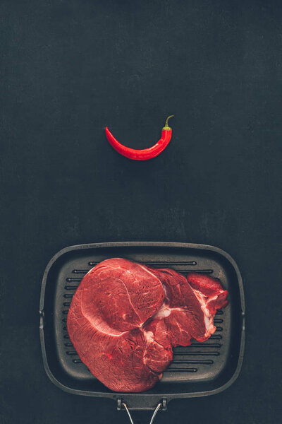 top view of raw steak on grill pan with chili pepper