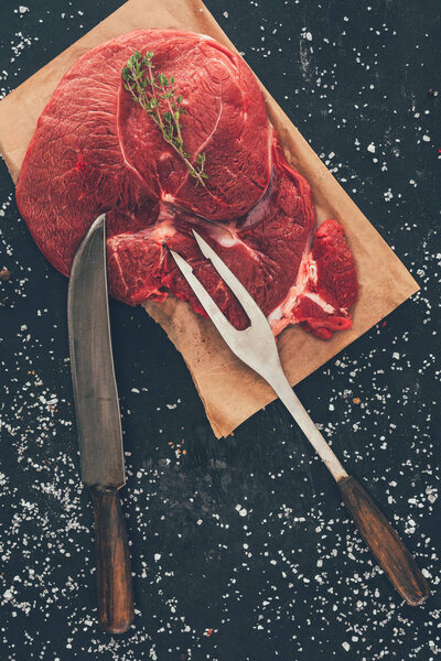 top view of raw steak with fork and knife on wooden board