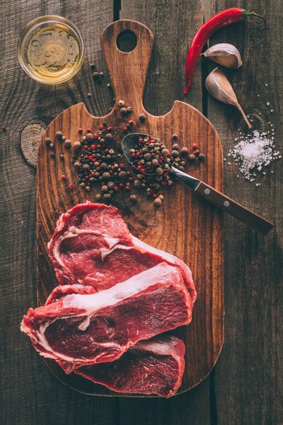 top view of heap of steaks with spices on wooden cutting board