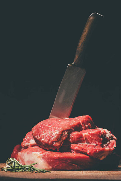 heap of raw steaks with knife on wooden board