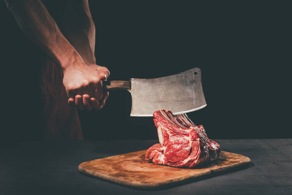 butcher cutting raw meat with cleaver on wooden cutting board