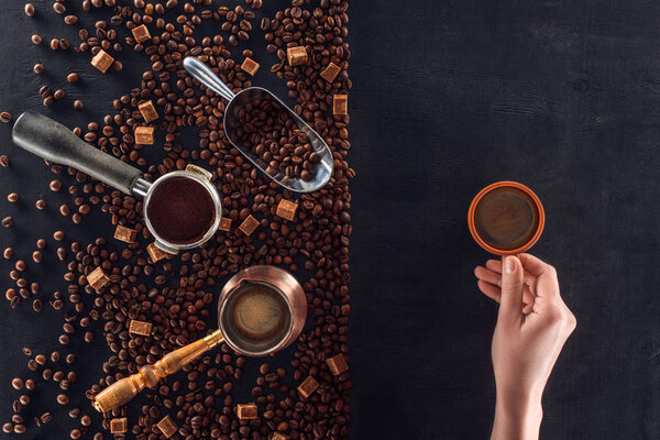 частичный вид лица, держащего чашку кофе и жареных кофейных зерен с кофейником, совок и сахар
 