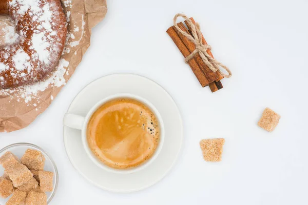 top view of cup of coffee with saucer and brown sugar, pastry and cinnamon sticks tied with rope isolated on white