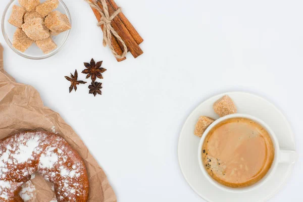 top view of cup of coffee with saucer and brown sugar, pastry, anise stars and cinnamon sticks tied with rope isolated on white 