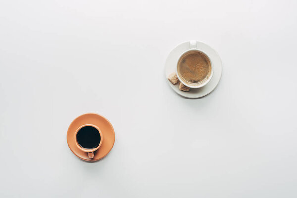 top view of two cups of coffee with saucers and brown sugar isolated on white 