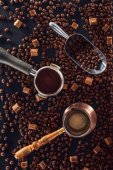 top view of roasted coffee beans, scoop, coffee tamper, coffee pot and brown sugar on black 