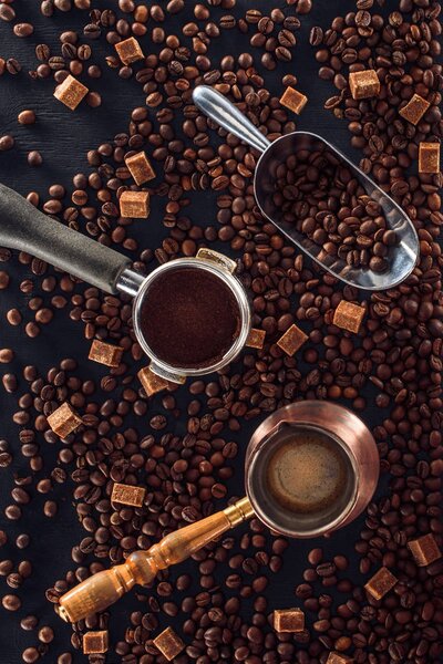 top view of roasted coffee beans, scoop, coffee tamper, coffee pot and brown sugar on black 