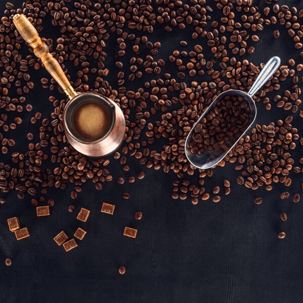 top view of roasted coffee beans, scoop and coffee pot on black