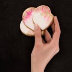 Tiro recortado de manos femeninas sosteniendo galletas en forma de corazón acristalado en el telón de fondo oscuro, San Valentín concepto de día