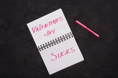 top view of notebook with valentines day sucks and pen on dark tabletop clipart