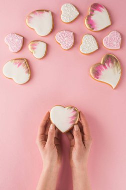 partial view of woman holding glazed cookie in hands isolated on pink, st valentines day concept clipart