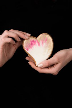 close up view of female hands with glazed heart shaped cookie isolated on black clipart