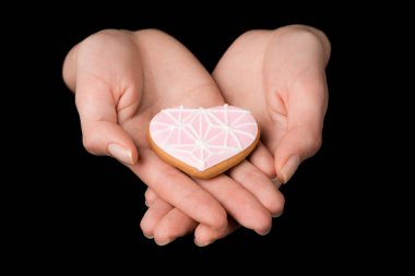 close up view of female hands with glazed heart shaped cookie isolated on black clipart