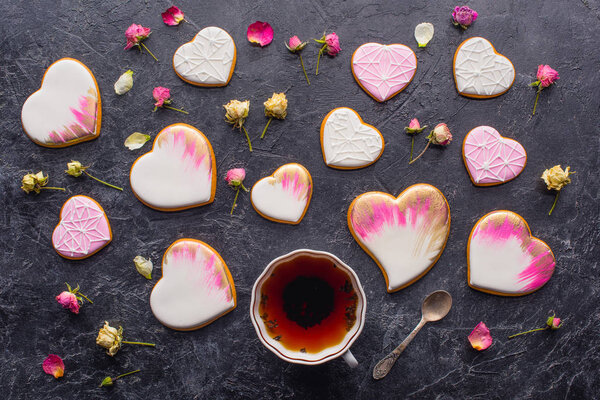st valentines day flat lay with cup of tea, glazed heart shaped cookies and decorative flowers on dark tabletop