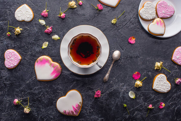 st valentines day flat lay with cup of tea, glazed heart shaped cookies and decorative flowers on dark tabletop