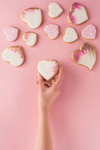 partial view of woman holding glazed cookie in hand isolated on pink, st valentines day concept