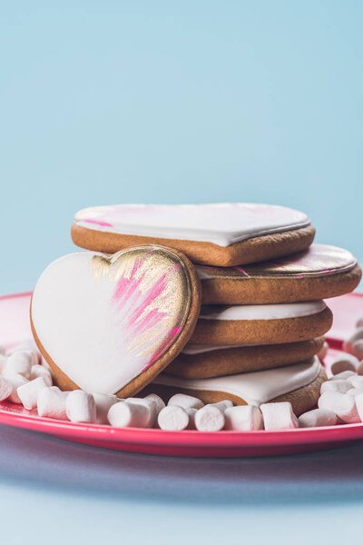 close up view of glazed cookies and marshmallow on pink plate isolated on blue