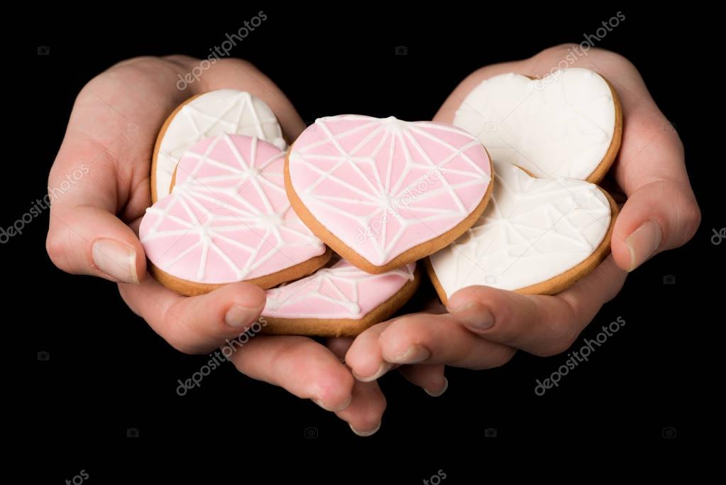 close up view of female hands with glazed heart shaped cookies isolated on black