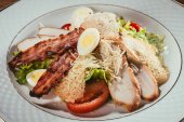 Nahaufnahme von köstlichem Salat mit Hühnerfleisch, Speck, Eiern und Käsedressing auf weißem Teller