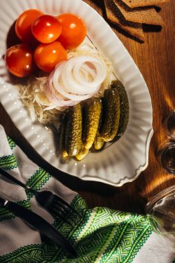 Top view of sauerkraut served with pickled vegetables on white plate on wooden table with napkin clipart
