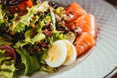 salad leaves mixed with vegetables laying on plate with some fish slices    clipart