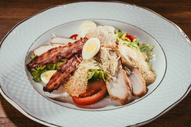 mixed leaf salad with ham slices and boiled eggs in plate over wooden surface 