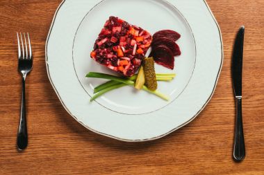 vinaigrette salad laying on plate over wooden table with fork and knife   clipart