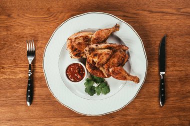 Top view of grilled chicken served on plate with sauce on wooden table clipart