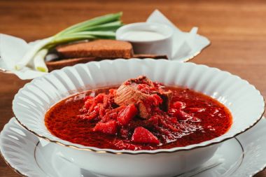 view of borsch soup with potato and meat in plate and green onions with bread and salt on background  clipart