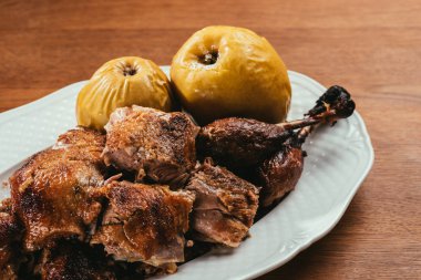 fried duck pieces laying on plate with marinated apples over wooden table    clipart