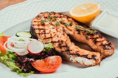 Yakın çekim görünümü ızgara Somon Balık adet limon, otlar ve beyaz tabak salataya 