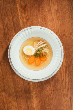 Top view of chicken soup with vegetables and egg in white plate on wooden table clipart
