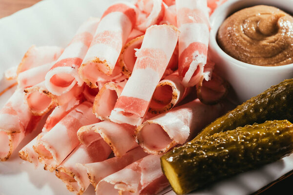 Close-up view of sliced bacon served with sauce and pickled cucumbers on plate