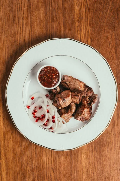 在木桌上的白色盘子上有洋葱 酱油和石榴籽的烤肉 — 图库照片