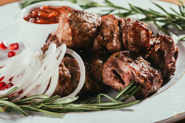 Close-up view of grilled meat with onion, rosemary and pomegranate seeds on white plate