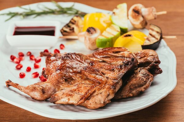 Close-up view of grilled vegetables on plate with fried chicken on wooden table