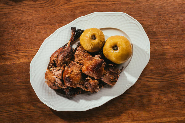 top view of fried duck pieces laying on plate with marinated apples over wooden table  