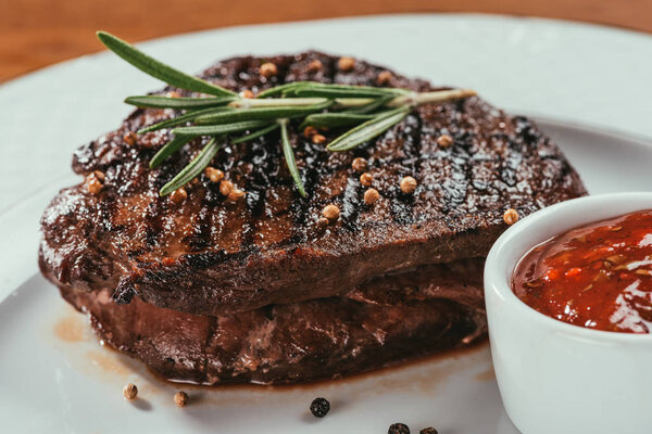 Close-up view of grilled steak with pepper, rosemary and sauce on white plate