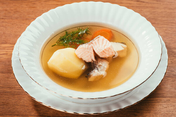 Hot soup with salmon and vegetables served in white plate on wooden table