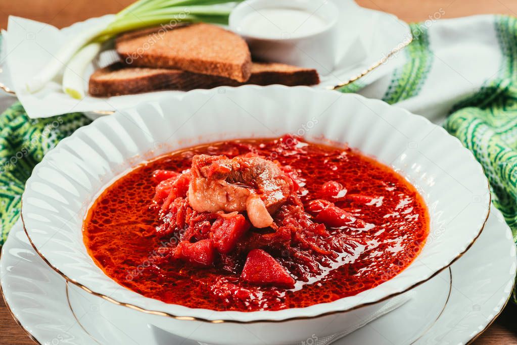 view of borsch soup with potato and meat in plate and green onions with bread and salt on background 