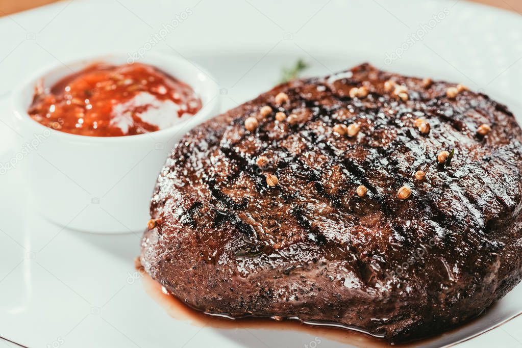 Close-up view of grilled steak with pepper and sauce on white plate