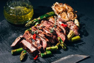 close-up view of tasty sliced grilled meat with asparagus, oil and spices on black clipart